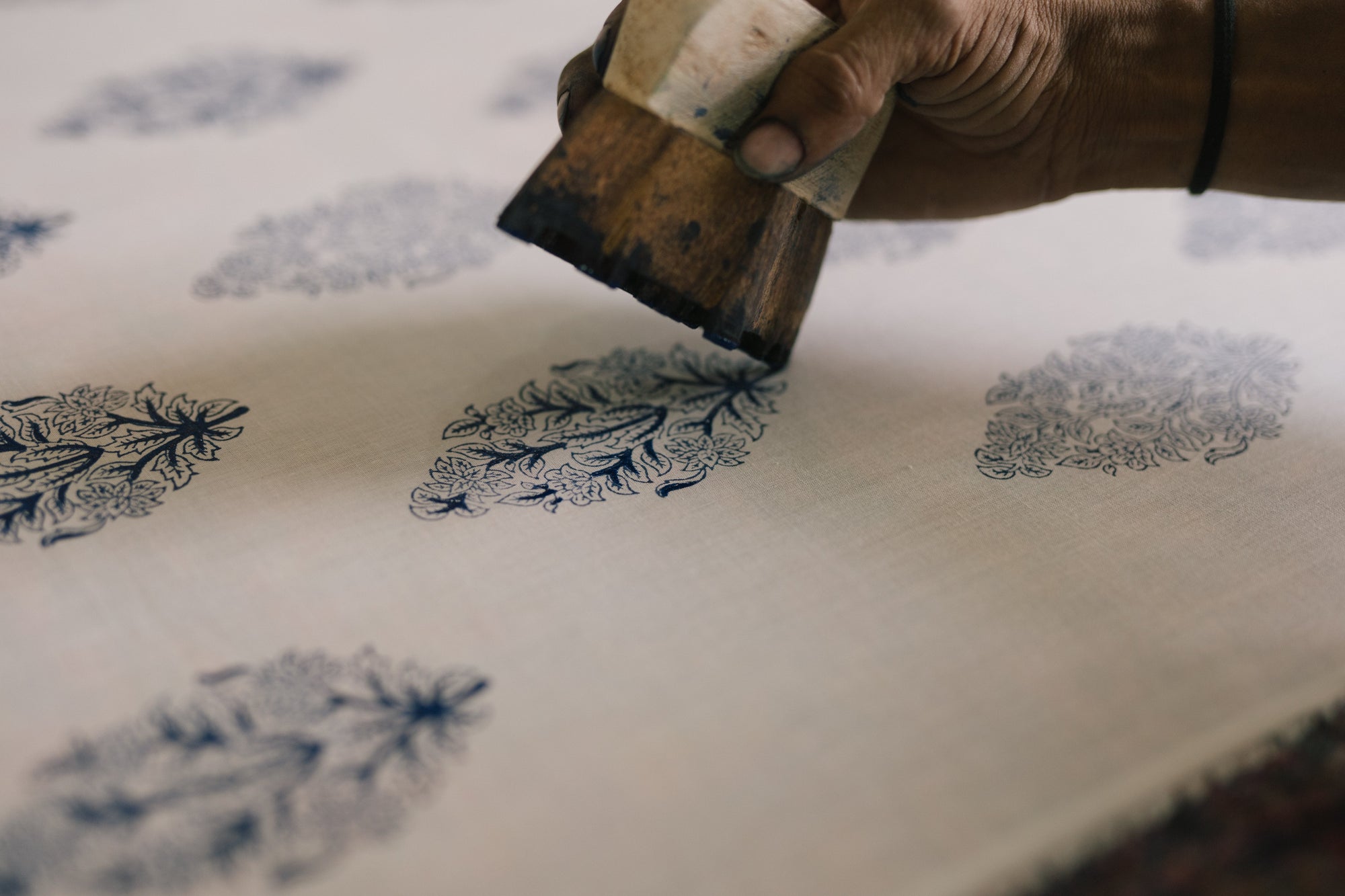Hand applying ink to a printing block with floral patterns on a white surface